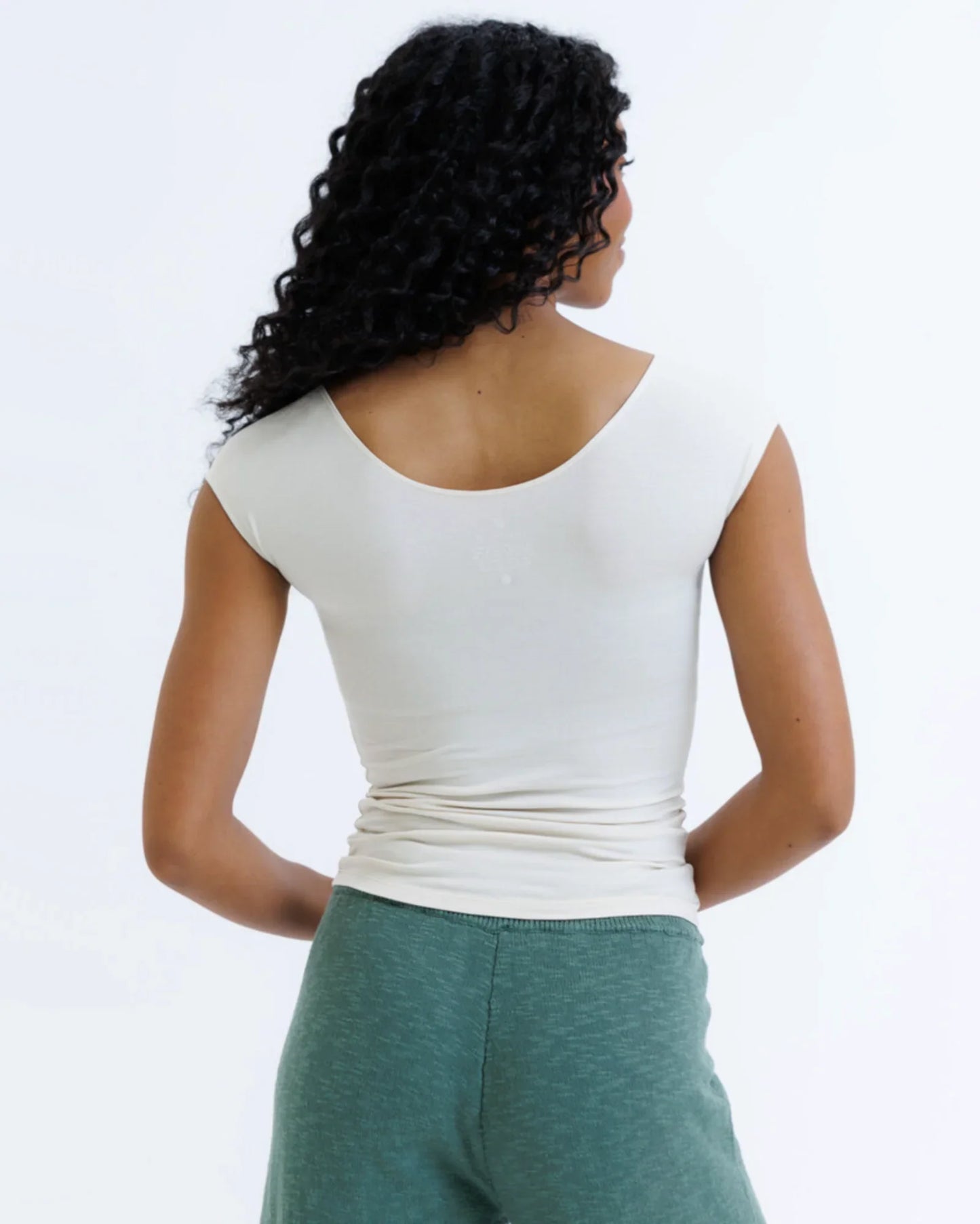 Woman wearing fitted white cap sleeve t-shirt and green lounge pants, shown from the back