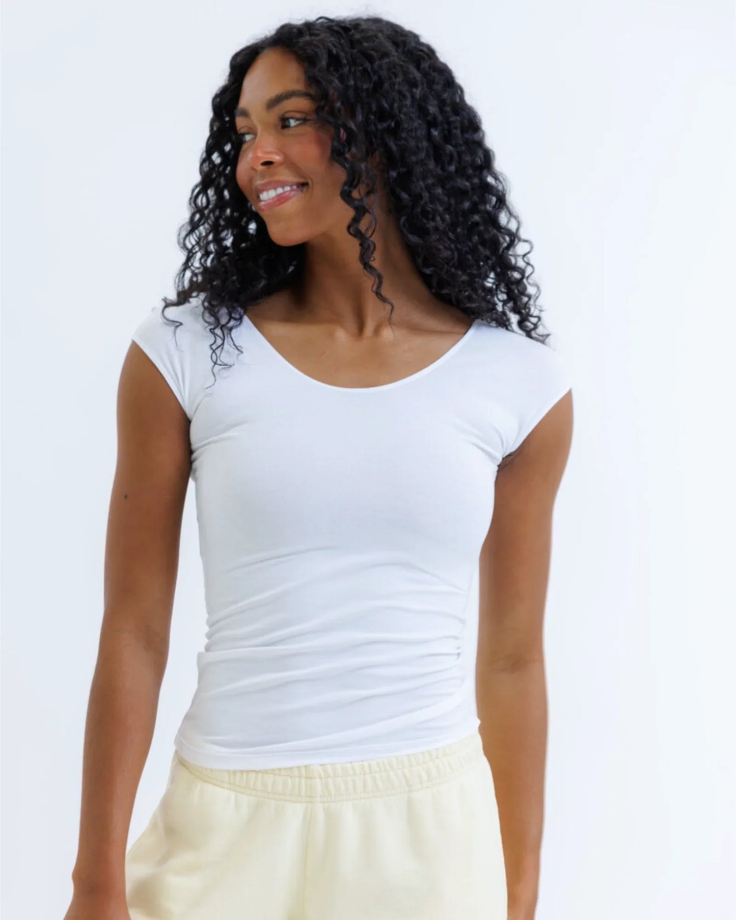 Woman wearing fitted white short sleeve tee and cream pants against light background