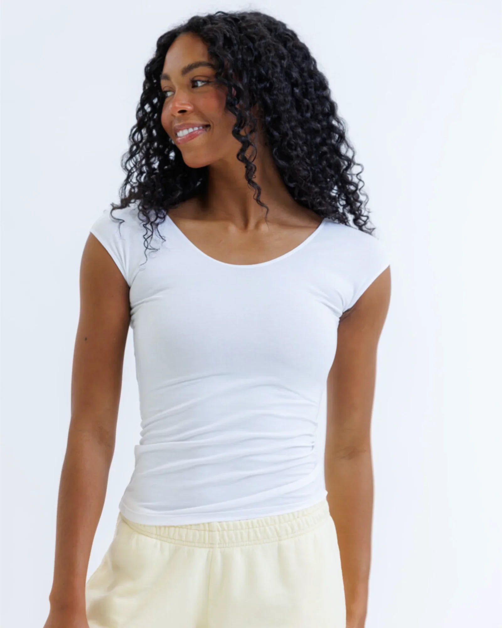 Woman wearing fitted white short sleeve tee and cream pants against light background