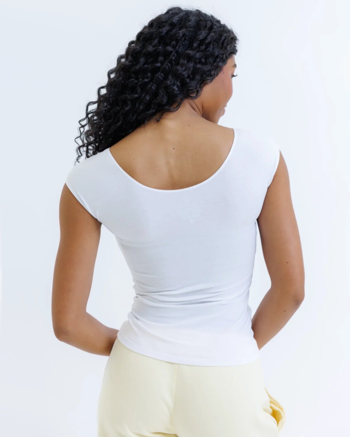 Woman wearing a fitted white short sleeve t-shirt and light yellow pants, back view