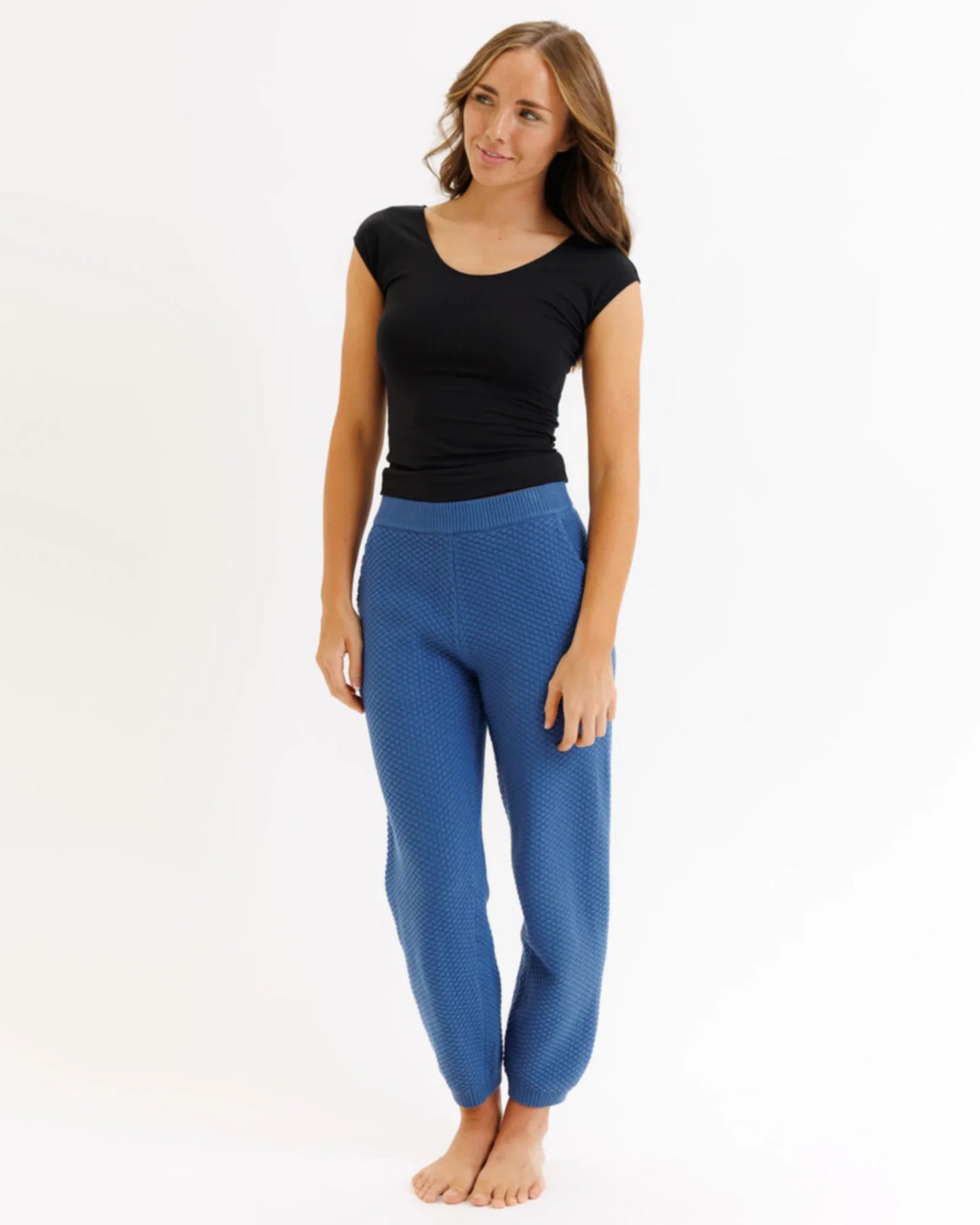Woman wearing a fitted black t-shirt and textured blue jogger pants on a white background