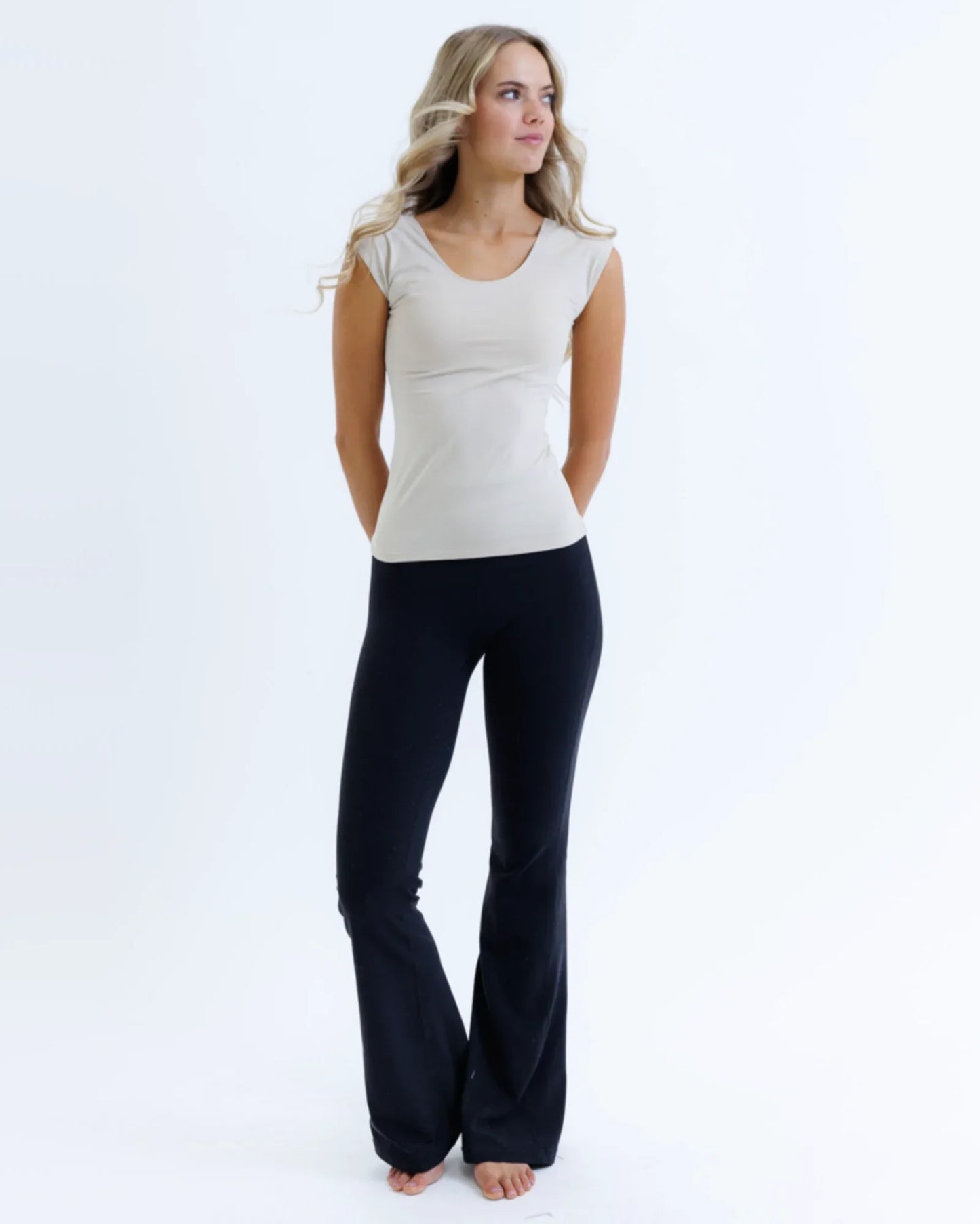 Woman wearing fitted nude essential tee and black flared pants, standing on white background